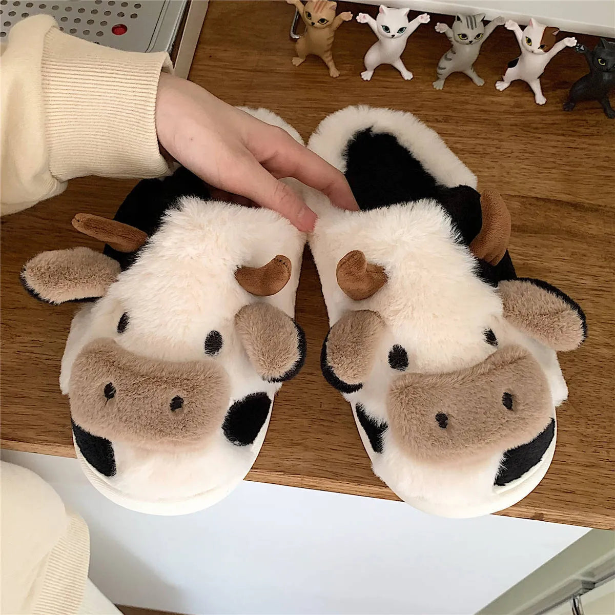 White cartoon cow plush slippers for women with a non-slip textured sole.
