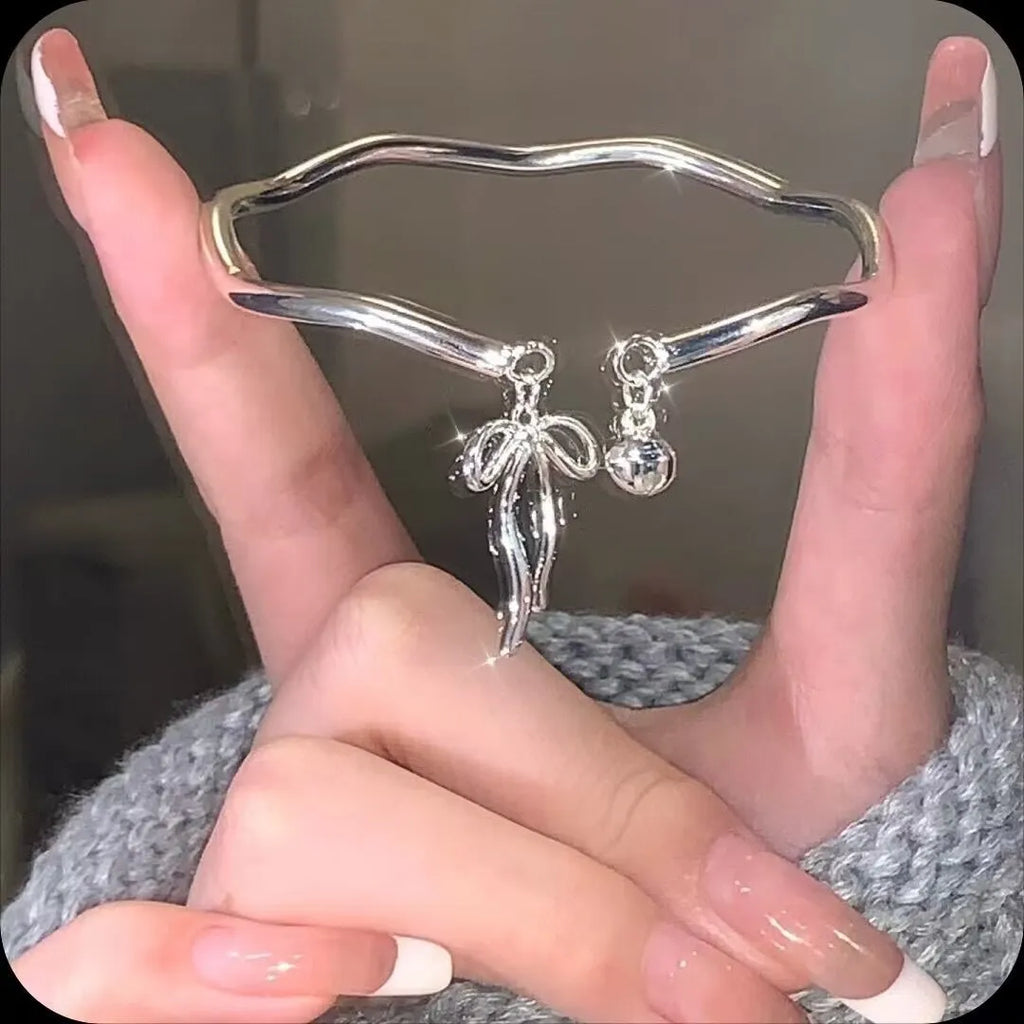 Silver adjustable bracelet with a bow charm and small bell on a zinc alloy band.