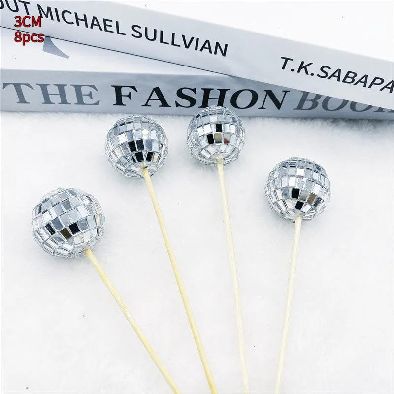 Glass disco ball cake decoration on wooden stick, showing reflective surface.
