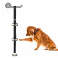 Silver metal dog training bells on an adjustable black nylon strap hanging from a door