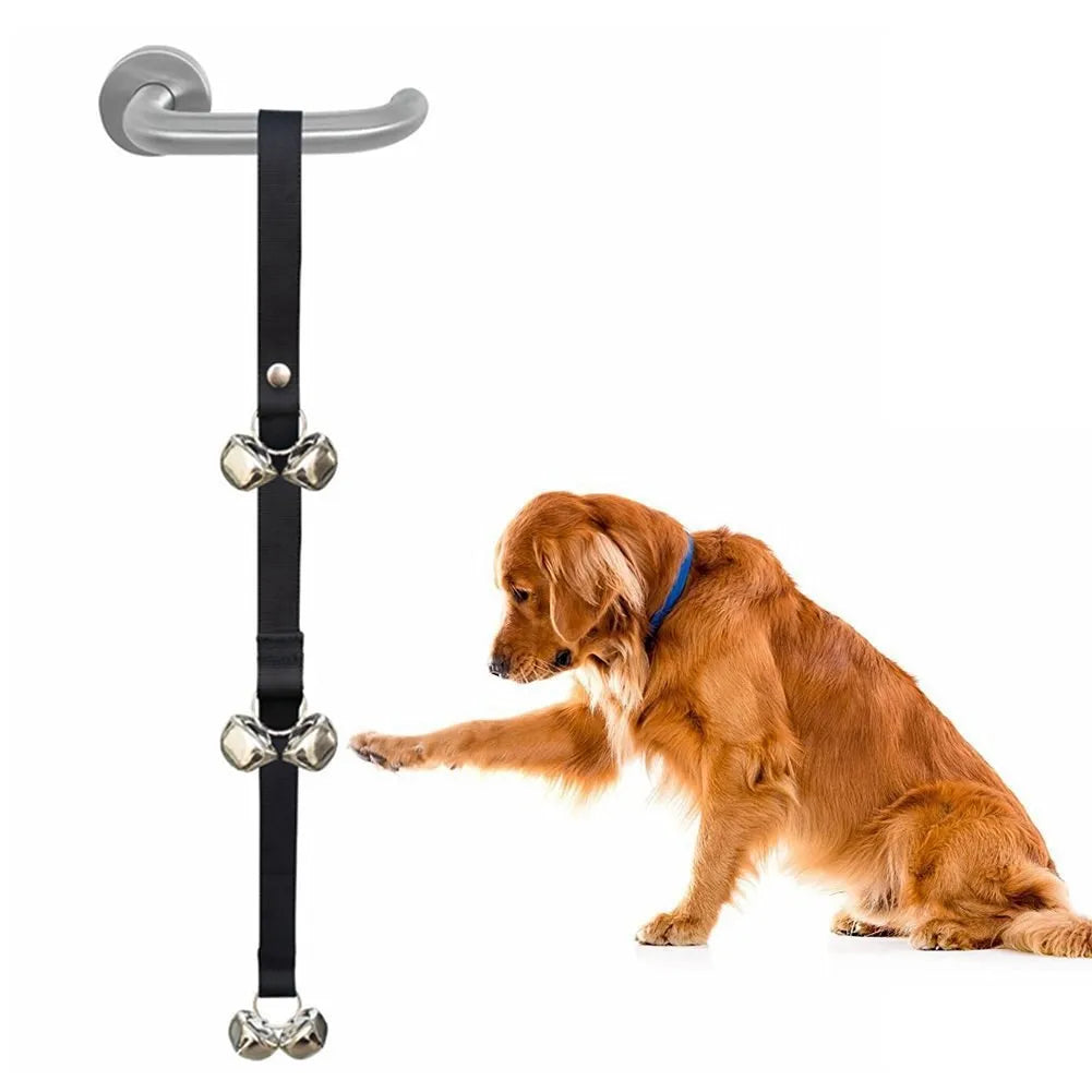 Silver metal dog training bells on an adjustable black nylon strap hanging from a door