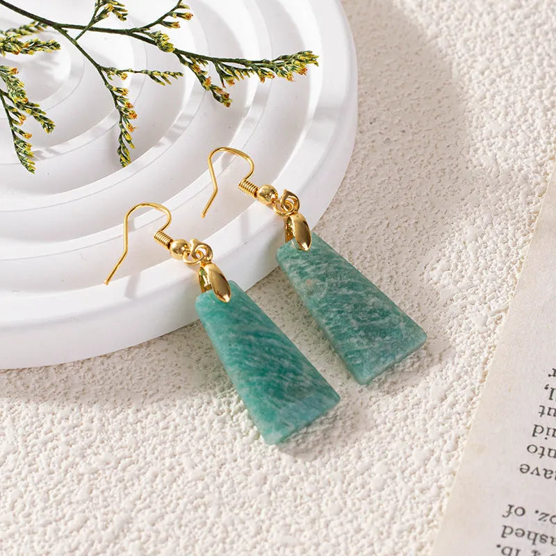 A pair of trapezoid-shaped earrings with a rough green amazonite stone set in a geometric gold or silver metal frame.