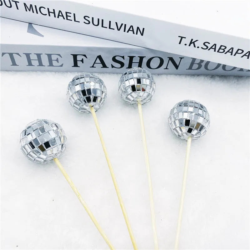 Glass disco ball cake decoration on wooden stick, showing reflective surface.