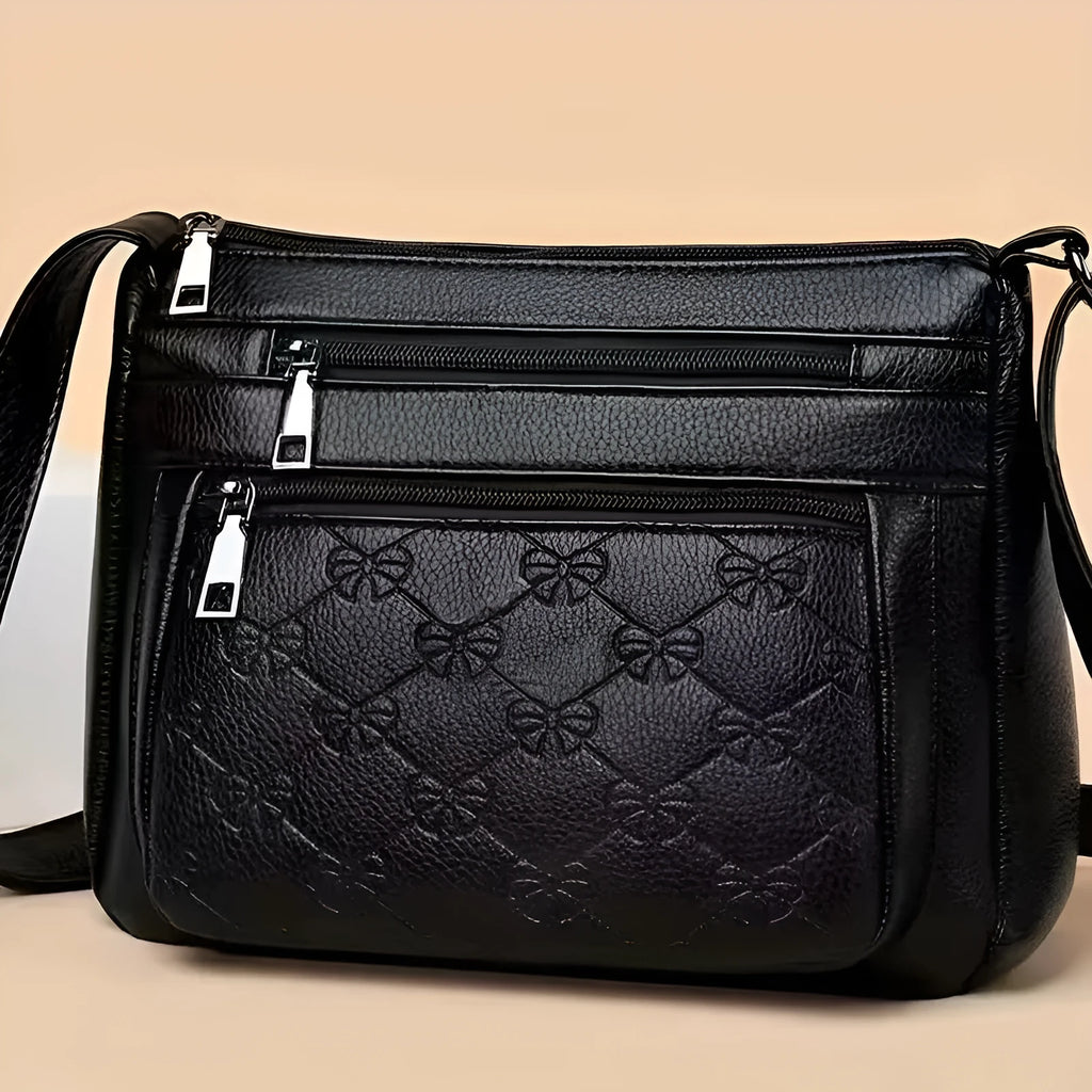 Black women's crossbody bag with embossed butterfly pattern showing phone pocket and external slit