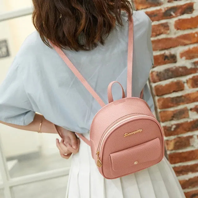 Small black PU leather women's shoulder backpack with a zipper, shown next to a mobile phone for scale.
