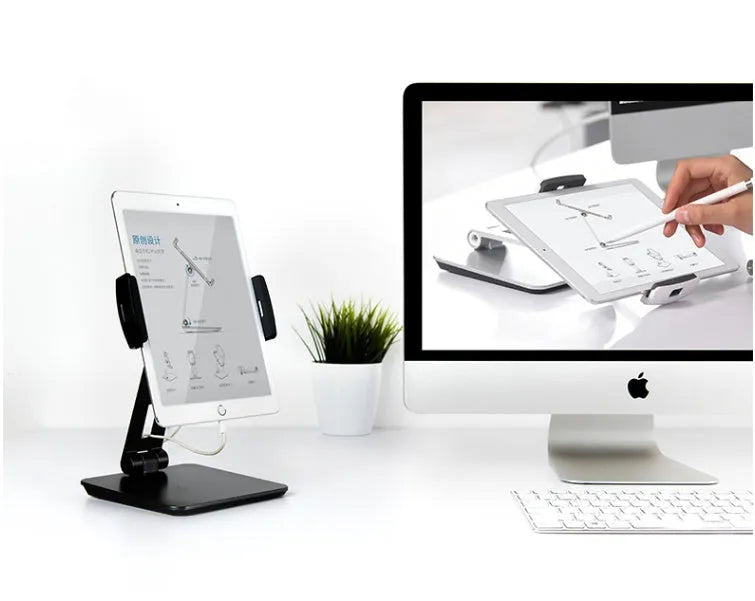 Silver foldable aluminium phone and tablet holder on a desk, showing 360-degree rotation feature.