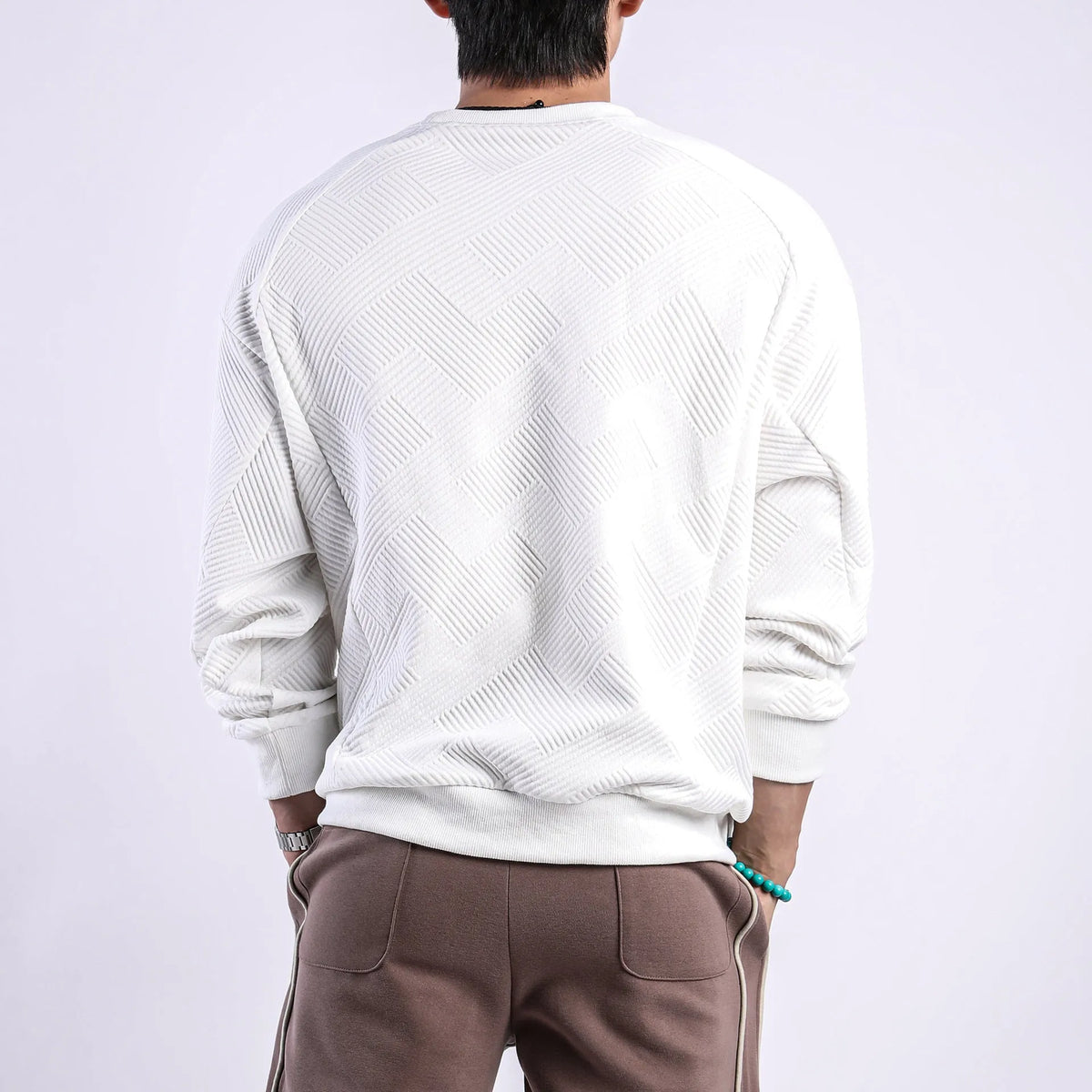 Man wearing a loose-fitting, long-sleeved army green pullover sweater with a textured twill jacquard pattern.