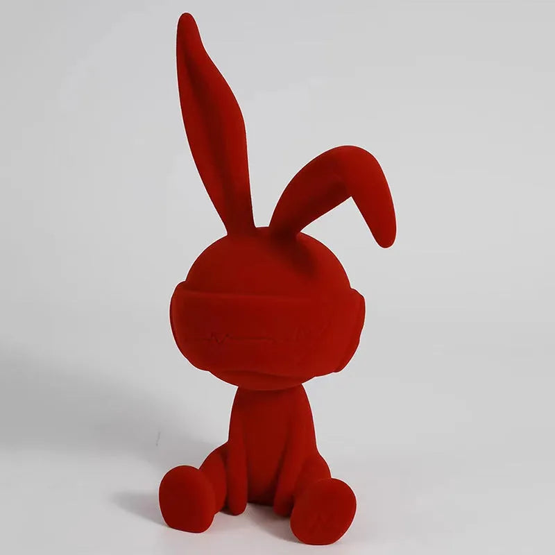 Resin table ornament of a rabbit wearing a suede blindfold with ribbon and tassel detail.