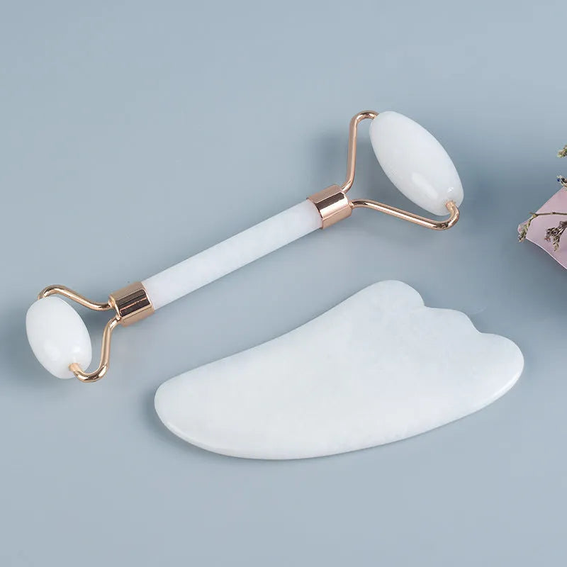 White jade double-headed facial roller and gua sha scraping board set on a plain background.