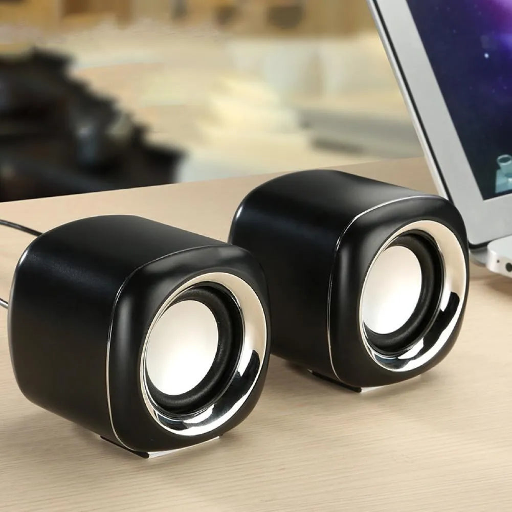 Pair of mini desktop speakers with 3.5mm audio plug on desk beside laptop
