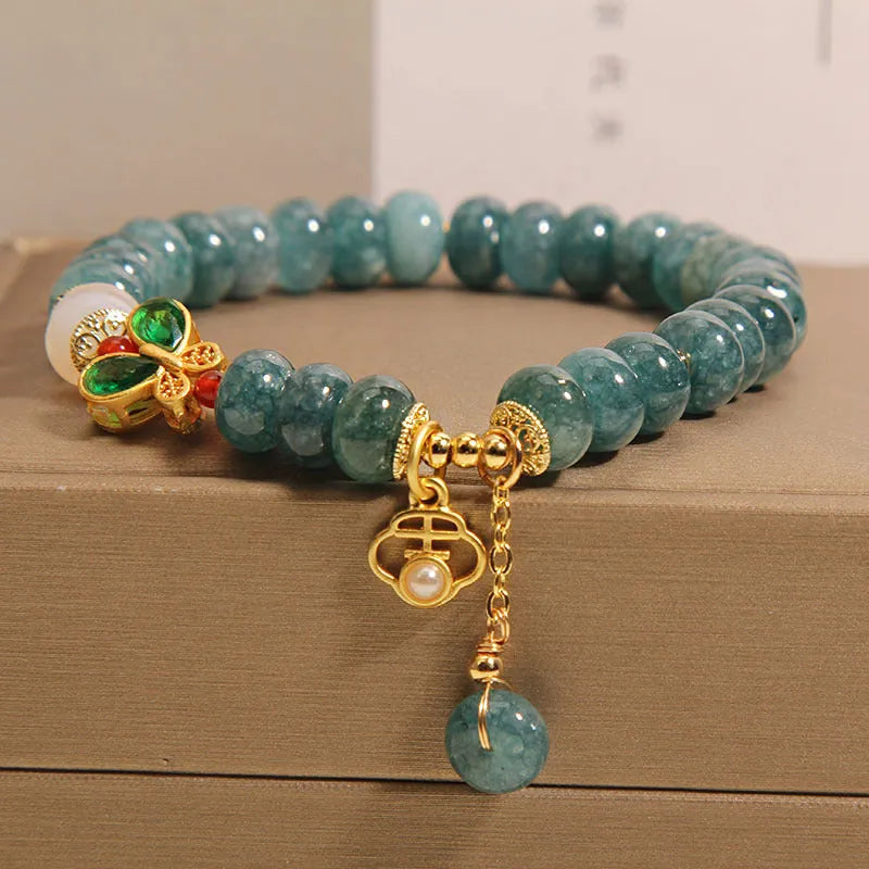 Close-up of a women's bracelet with blue jade and white agate abacus beads, butterfly charms, and rhinestones on an alloy chain.