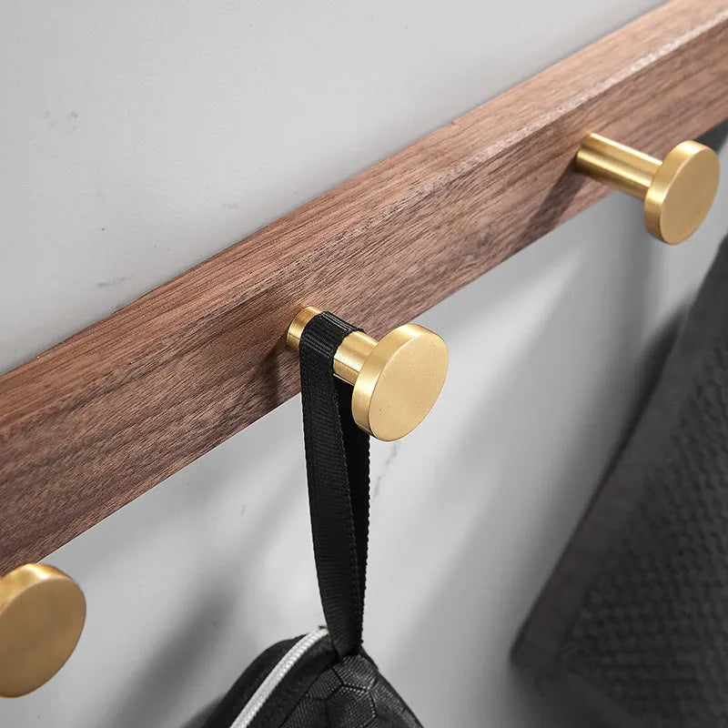 A row of black walnut aluminium wall hooks with a brass wire drawing finish, shown in a bathroom setting.