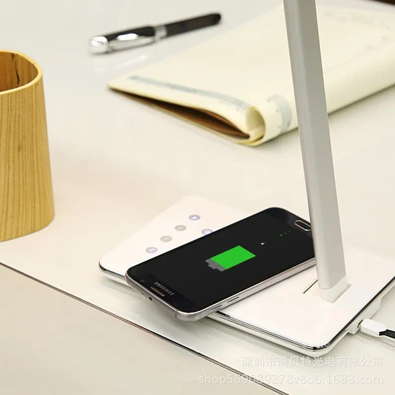 Black wireless charging desk lamp with touch switch and USB cable on a wooden desk.