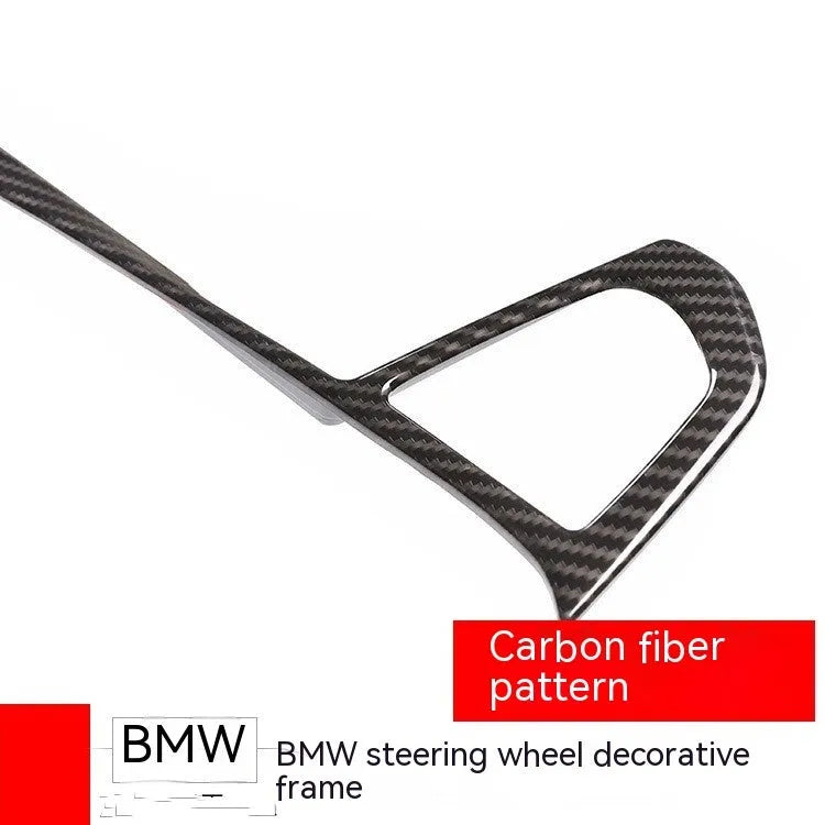 Black carbon fibre pattern button frame for BMW steering wheel, shown as a single clip-on trim piece.