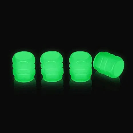 Set of luminous green rubber tyre valve caps on a car wheel valve stem, glowing in low light.