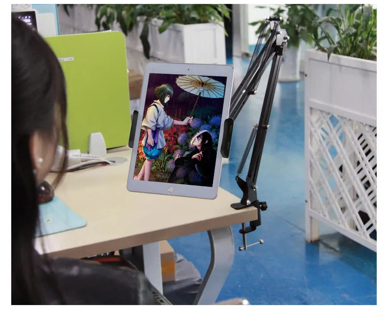 Black adjustable phone tablet stand with 360-degree rotating head on wooden desk