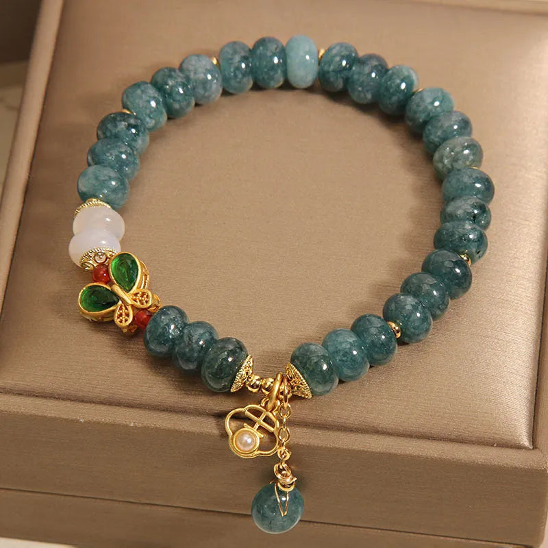 Close-up of a women's bracelet with blue jade and white agate abacus beads, butterfly charms, and rhinestones on an alloy chain.