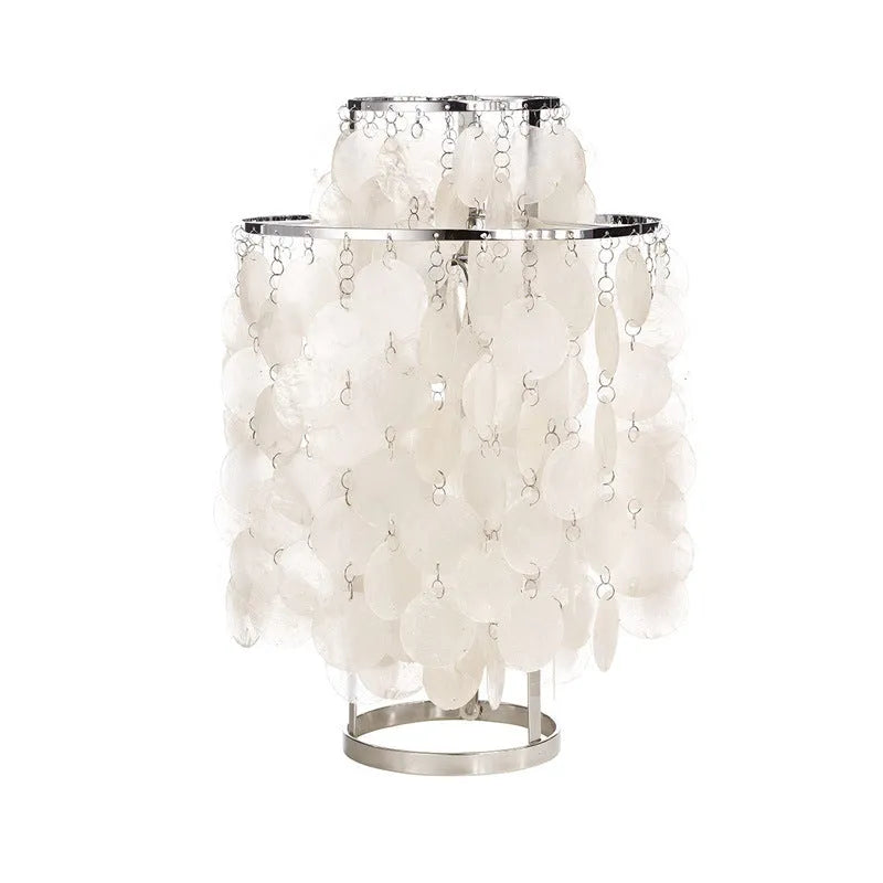 Modern shell-shaped metal bedside table lamp in chrome finish on a wooden table.