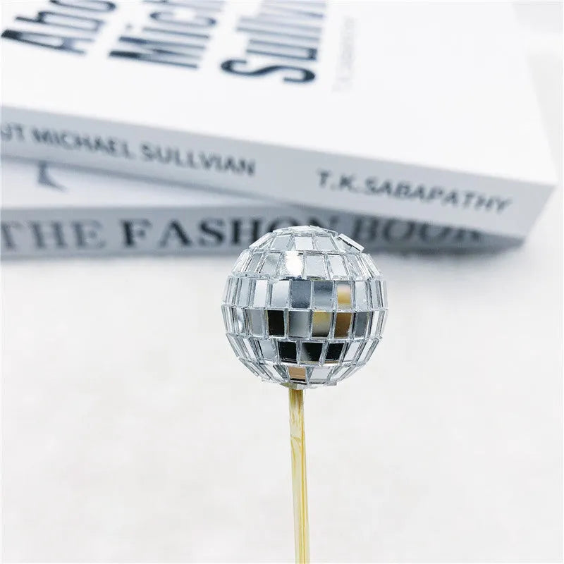 Glass disco ball cake decoration on wooden stick, showing reflective surface.