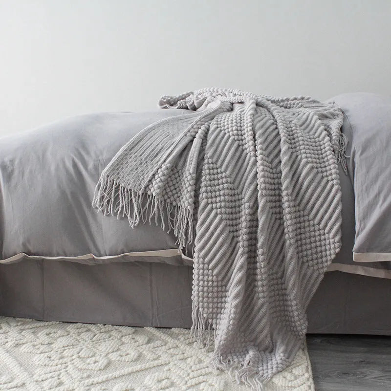 Small light grey polyester blanket folded on a sofa