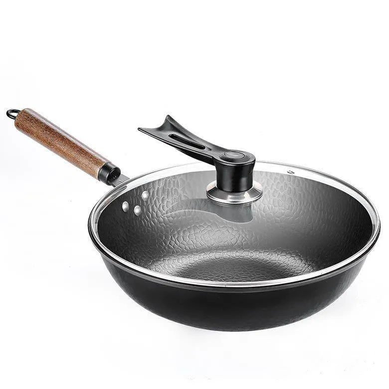 Black traditional cast iron wok pan with wooden handle and glass lid on induction hob