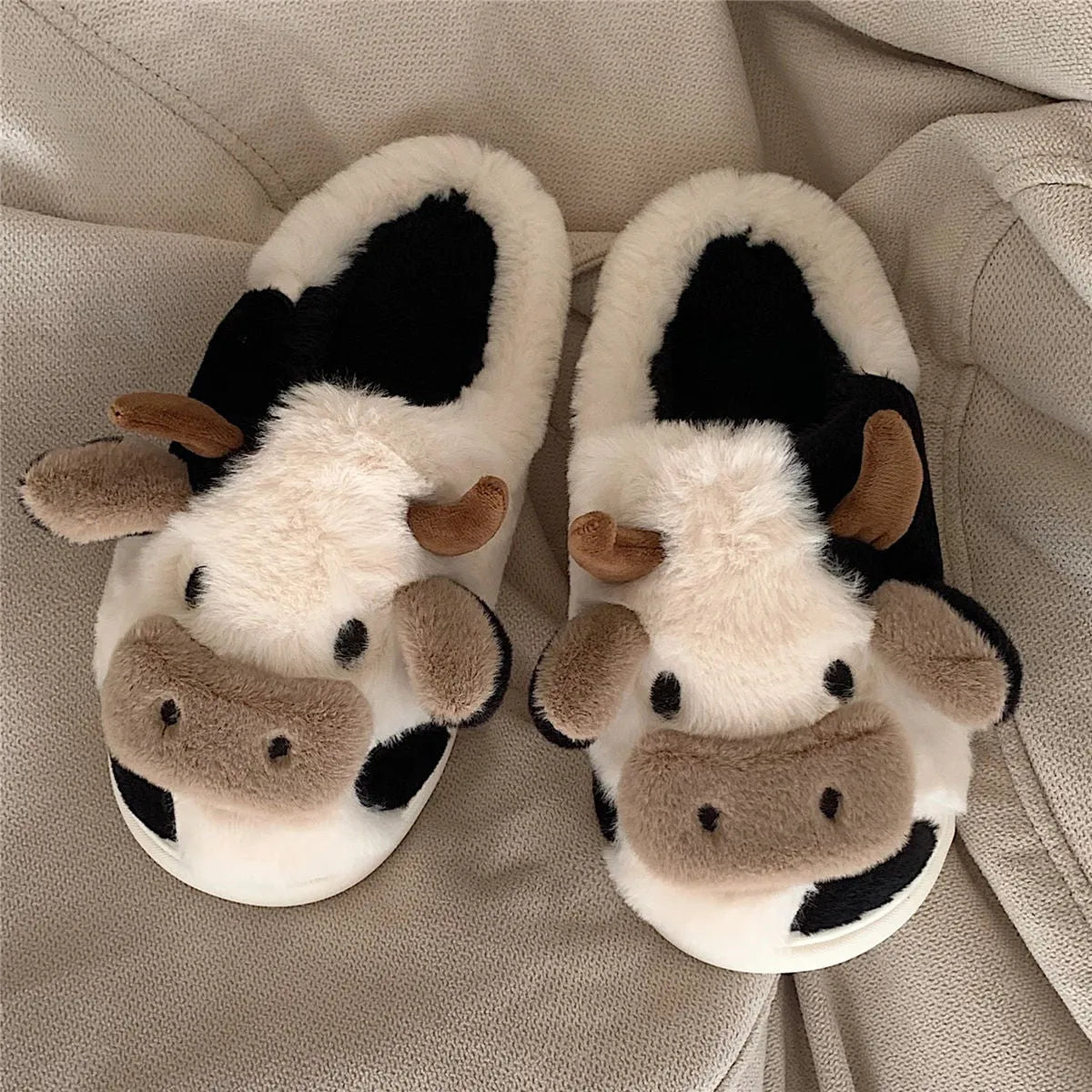 White cartoon cow plush slippers for women with a non-slip textured sole.