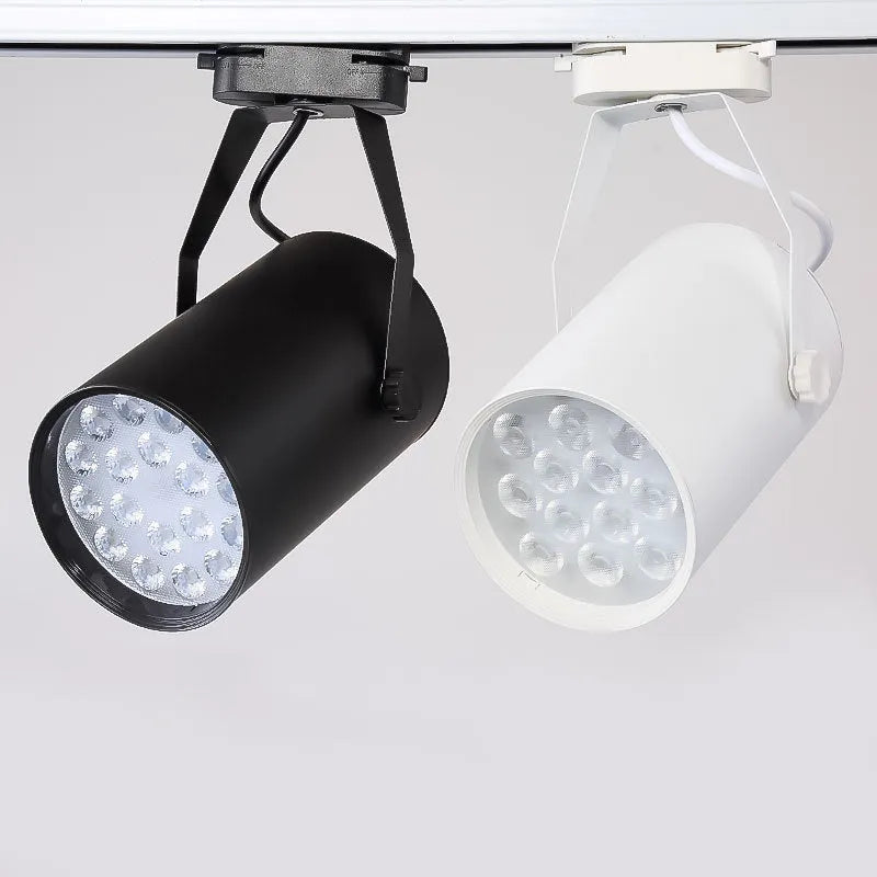A black aluminium LED track spotlight mounted on a lighting track, angled to illuminate a wall.
