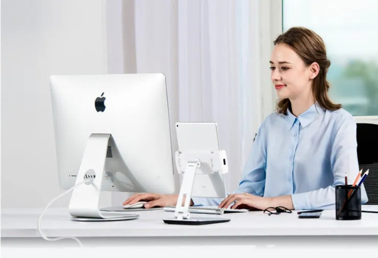 Silver foldable aluminium phone and tablet holder on a desk, showing 360-degree rotation feature.