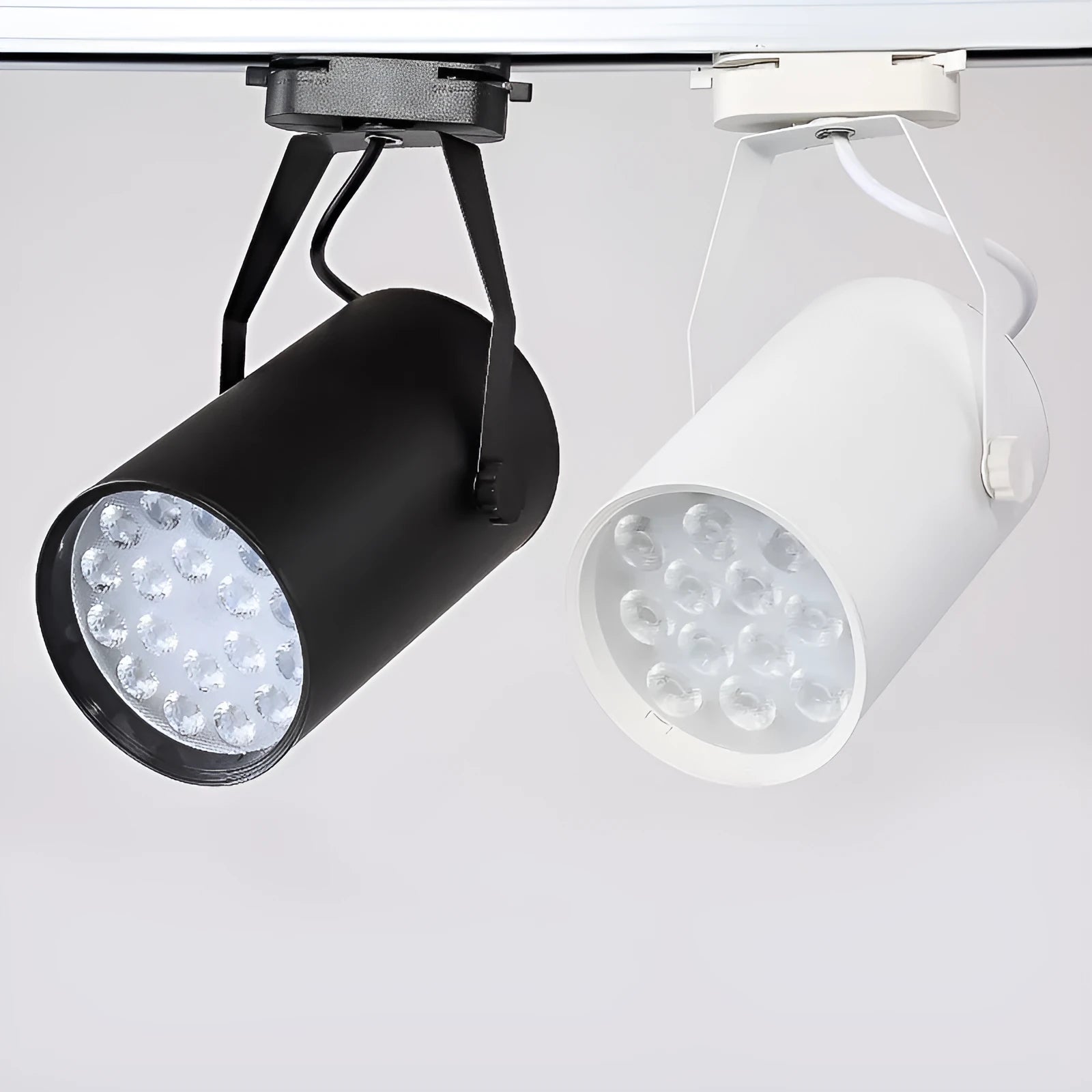 A black aluminium LED track spotlight mounted on a lighting track, angled to illuminate a wall.