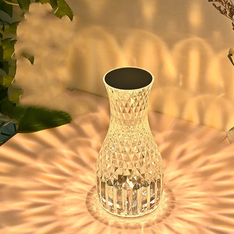 Transparent vase-shaped crystal LED table lamp with multi-colour lights on a wooden table.
