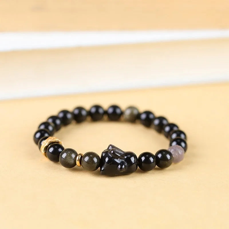 Handmade lying rabbit obsidian bracelet with grey agate beads and brass details on a wrist.