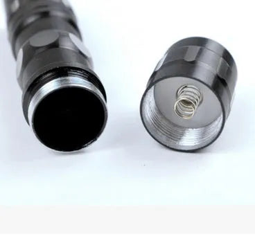 Small black aluminium LED mini flashlight with strong beam, shown next to a AA battery for scale.