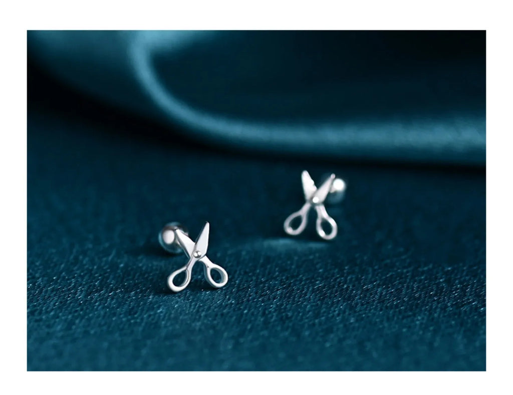 A pair of silver screw-back ear nails with a miniature scissors design on the screw component.