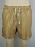 Man wearing grey striped polyester beach shorts with a straight leg opening, on a beach.