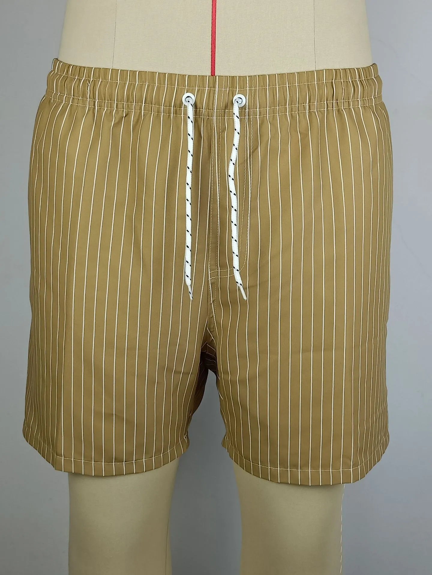 Man wearing grey striped polyester beach shorts with a straight leg opening, on a beach.