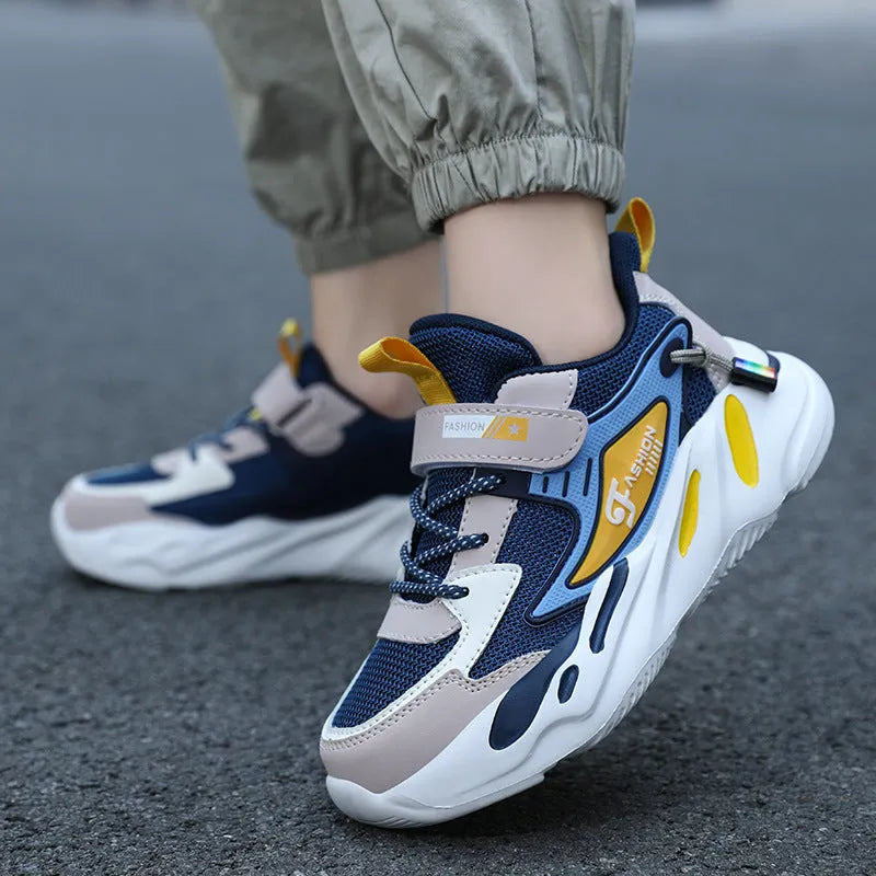 Boys' blue and black platform sports running shoes with Velcro straps on a hard ground surface.