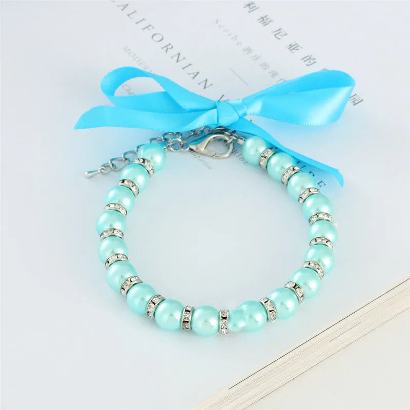 Small dog wearing an adjustable blue pearl and rhinestone necklace with a ribbon bow on a soft ribbon.