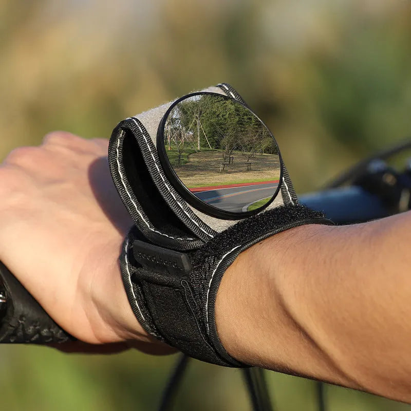 Black nylon wrist-mounted bicycle rear-view mirror with velcro strap and armoured glass reflective surface.