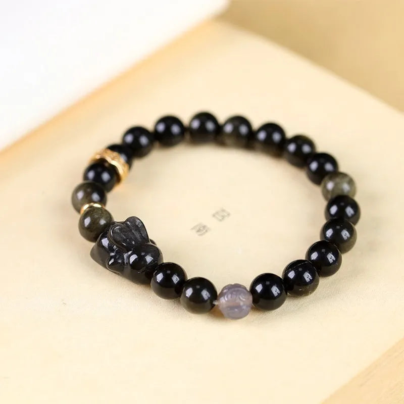 Handmade lying rabbit obsidian bracelet with grey agate beads and brass details on a wrist.