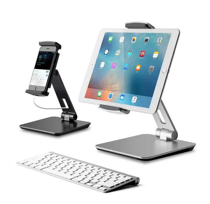 Silver foldable aluminium phone and tablet holder on a desk, showing 360-degree rotation feature.