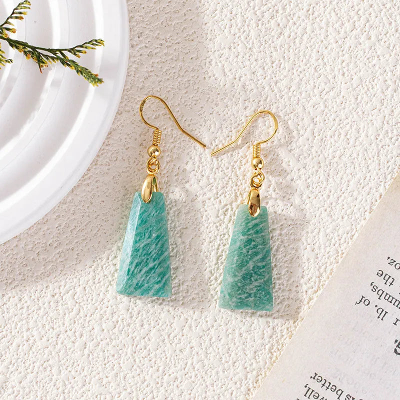 A pair of trapezoid-shaped earrings with a rough green amazonite stone set in a geometric gold or silver metal frame.