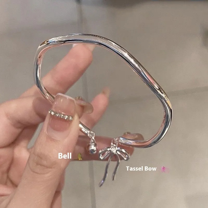 Silver adjustable bracelet with a bow charm and small bell on a zinc alloy band.