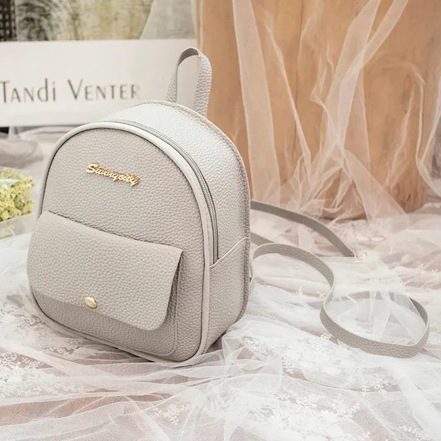 Small black PU leather women's shoulder backpack with a zipper, shown next to a mobile phone for scale.