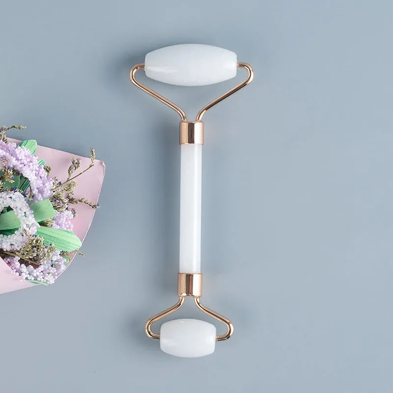 White jade double-headed facial roller and gua sha scraping board set on a plain background.