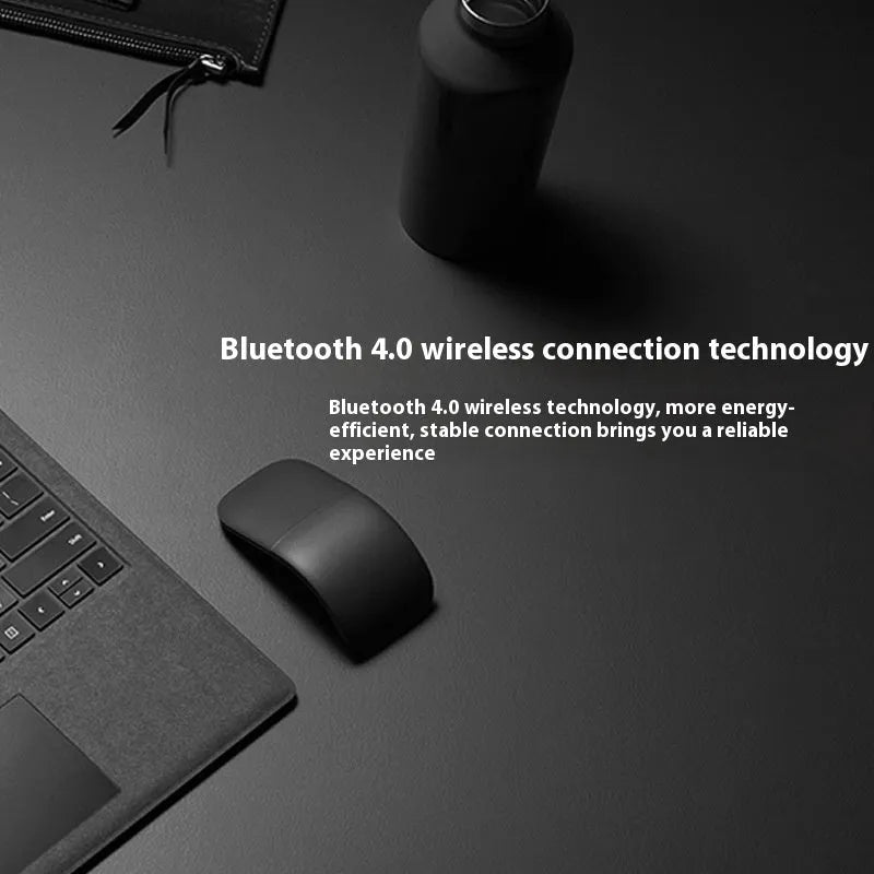A closed black folding Bluetooth wireless mouse showing its compact size next to a laptop.