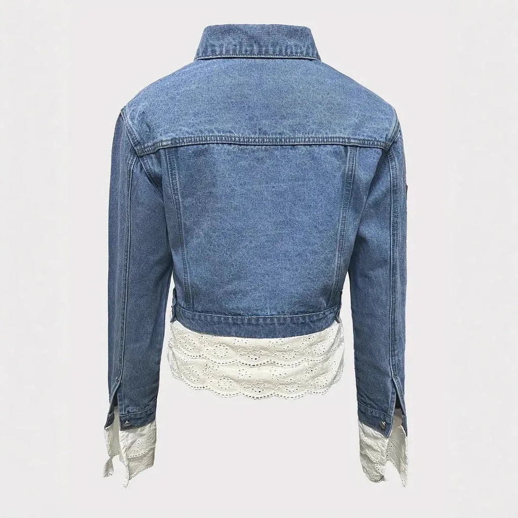 Blue women's denim jacket with lace stitching on the front, shown on a hanger.