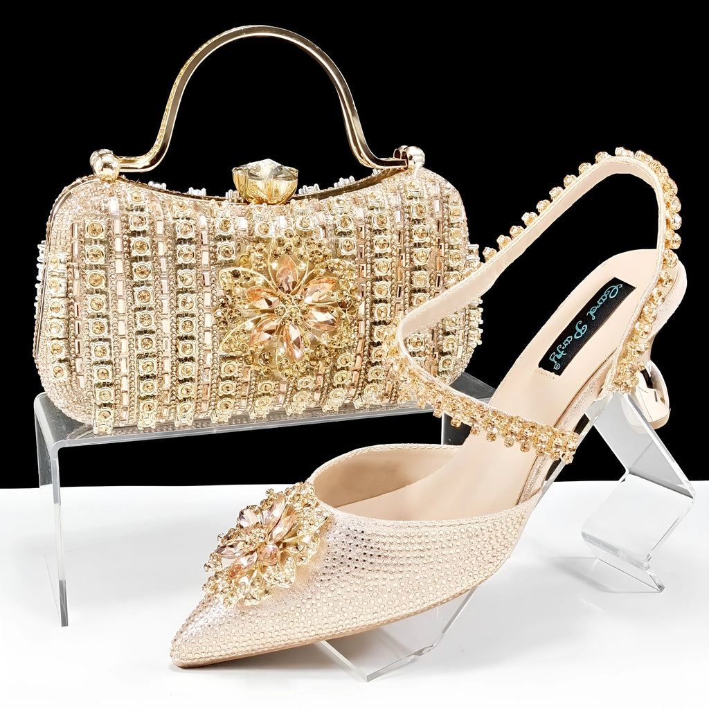 Women's black high heel sandal with rhinestone flower decoration and ankle chain, shown with matching clutch bag
