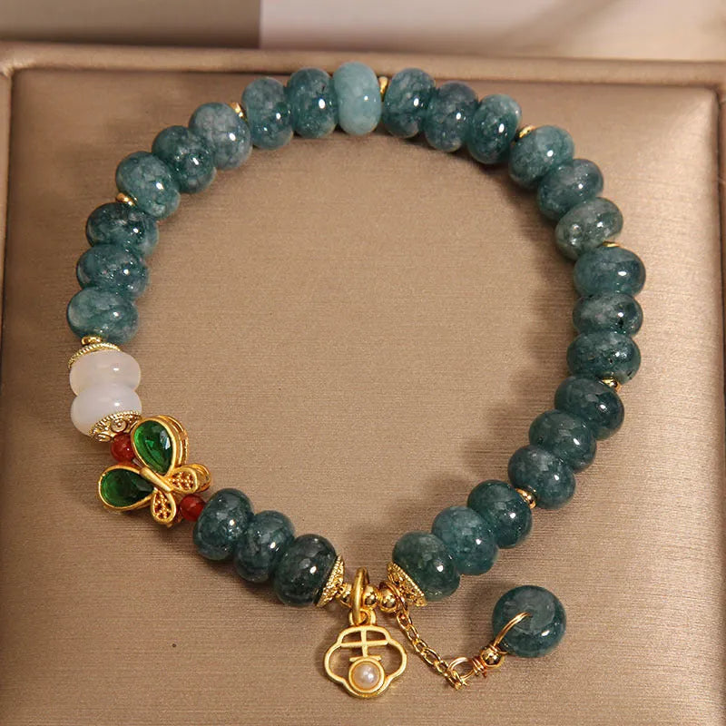 Close-up of a women's bracelet with blue jade and white agate abacus beads, butterfly charms, and rhinestones on an alloy chain.