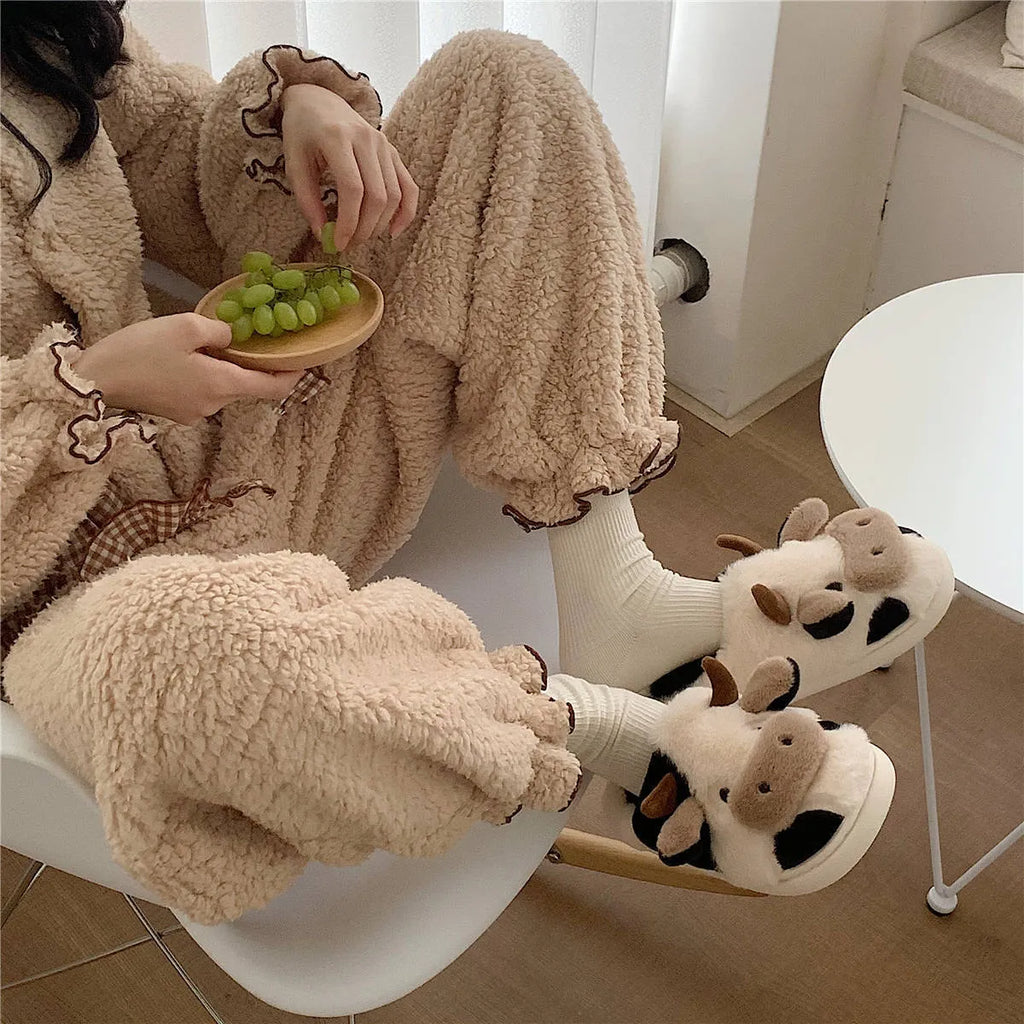 White cartoon cow plush slippers for women with a non-slip textured sole.