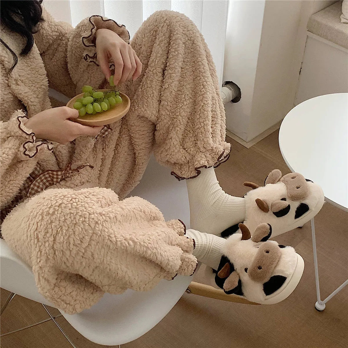 White cartoon cow plush slippers for women with a non-slip textured sole.